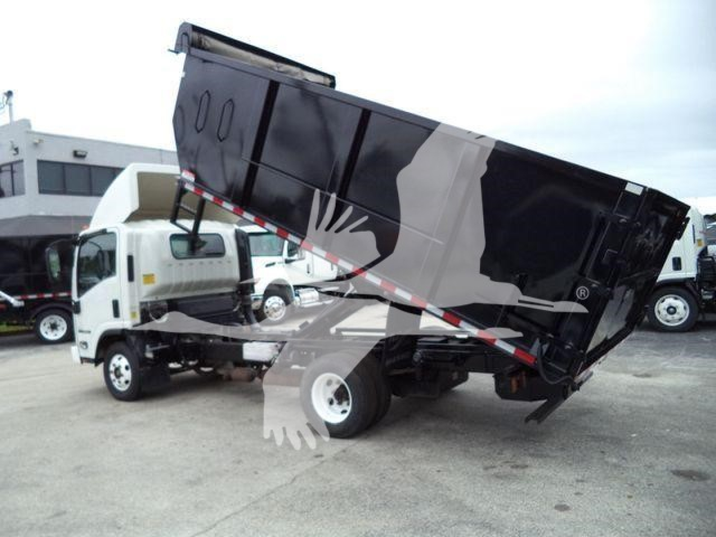 Isuzu NPR dump truck with tilted black hopper in a parking lot.