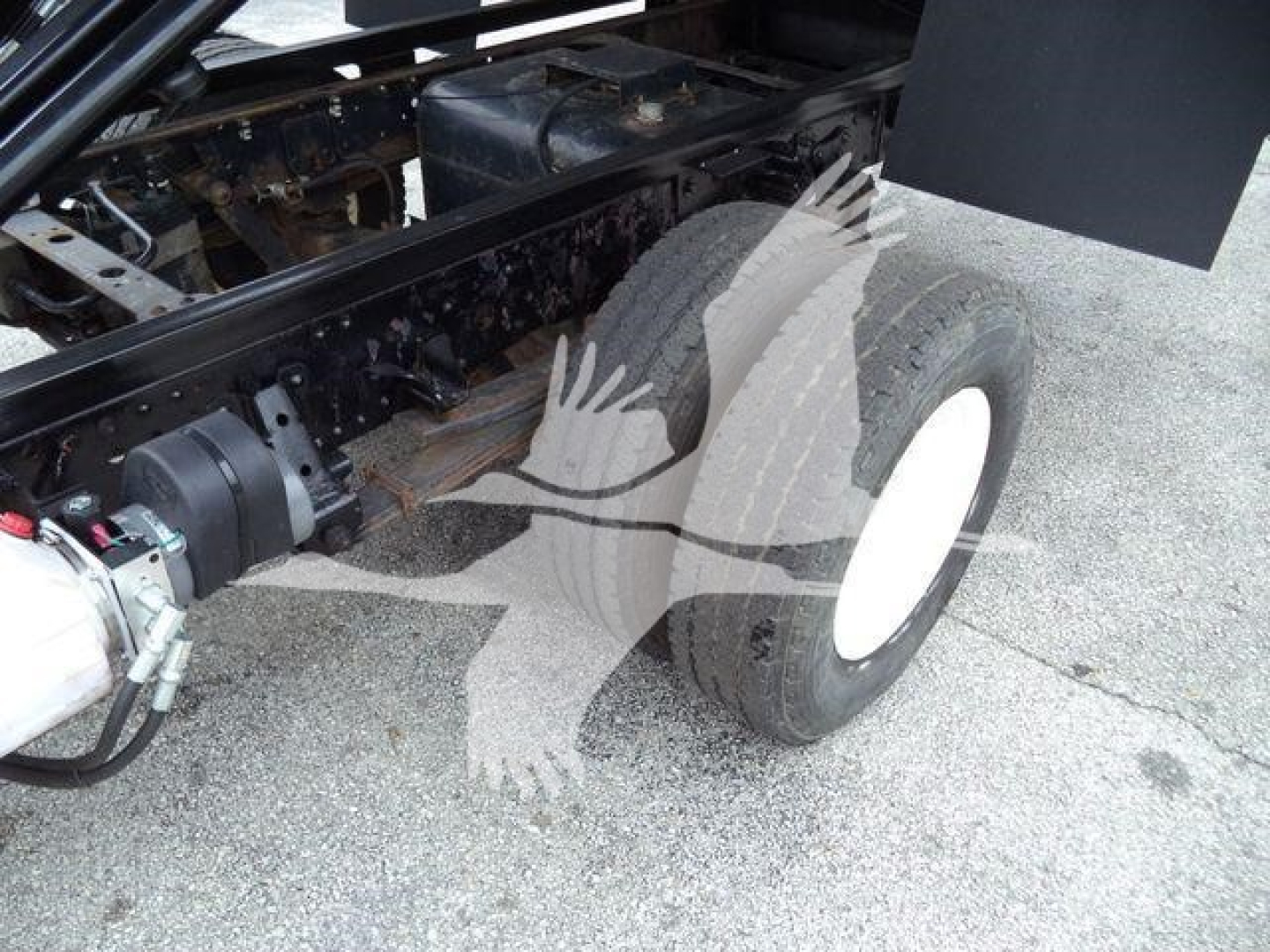 Isuzu NPR truck chassis showing front wheel and undercarriage with hydraulic lines and frame, no engine visible.