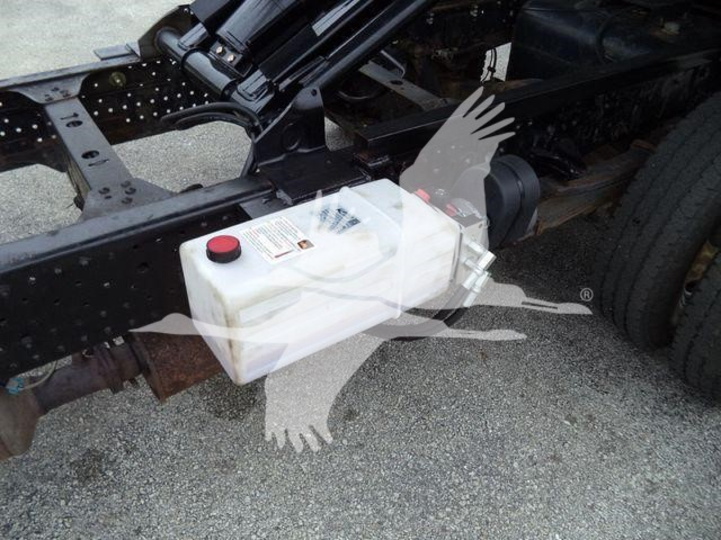 Isuzu NPR truck chassis showing white plastic reservoir tank with red cap mounted under frame.
