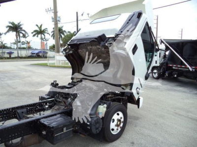 Isuzu NPR truck cab tilted up showing engine bay area and front wheel with surrounding chassis.