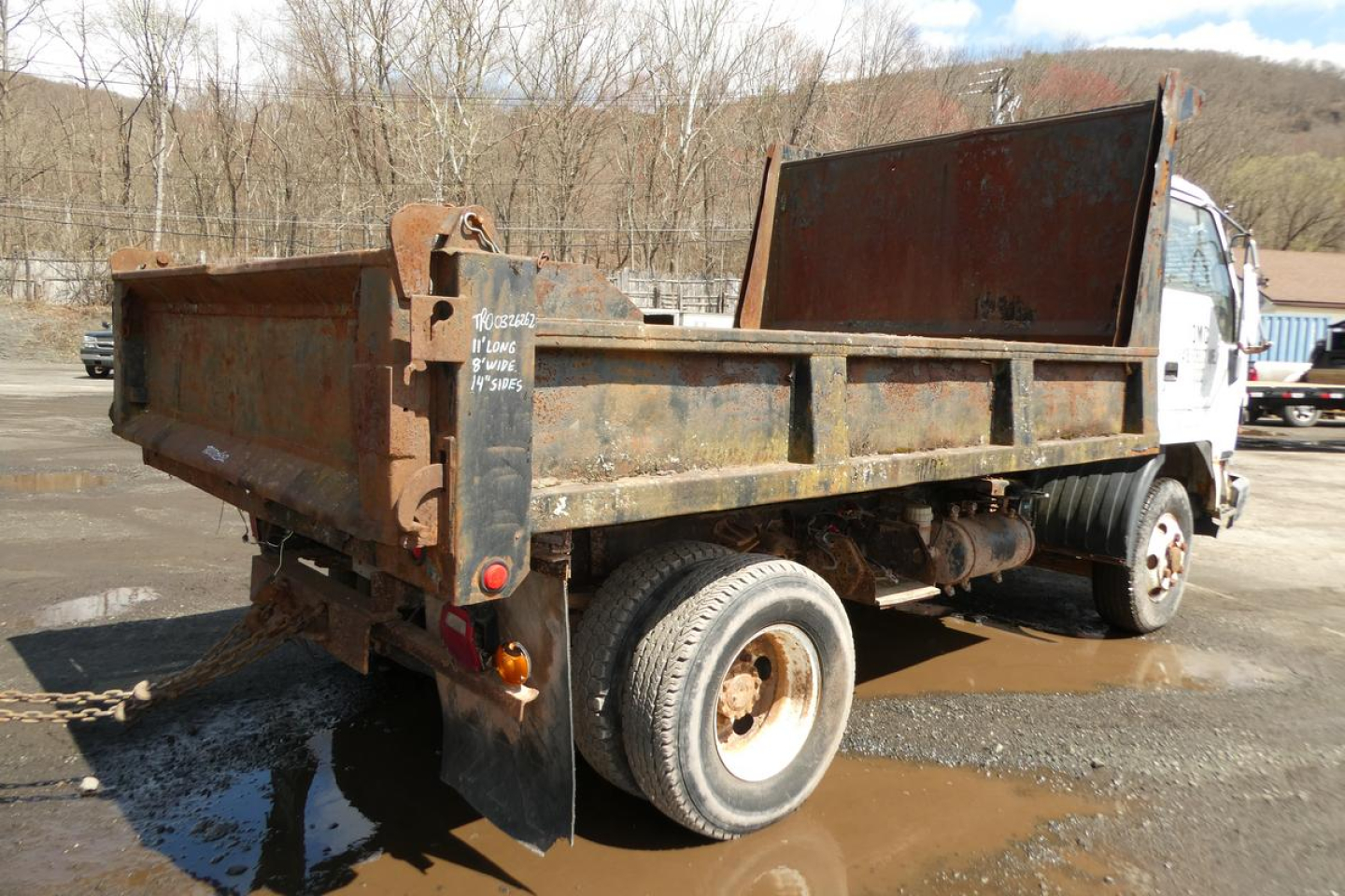 Truck bed of a 1993 Mitsubishi FH dump truck with rusted metal dump box and rear tailgate, chassis and single rear wheel visible.