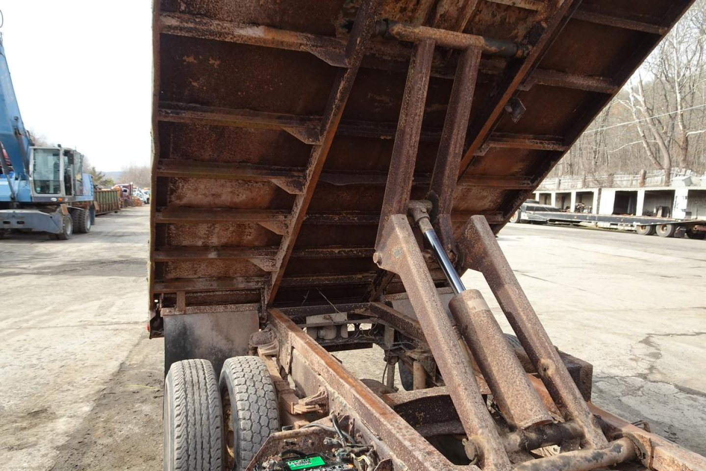 Dump truck trailer bed raised showing hydraulic rams and rusty metal frame and dual rear wheels.