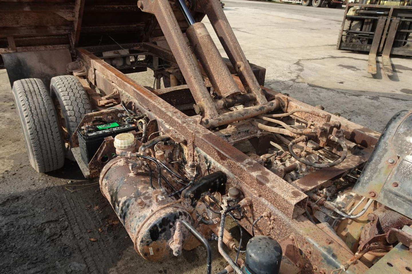 Chassis and hydraulic arm assembly of a Mitsubishi FH dump truck frame showing exposed metal components and a rusty, weathered frame.