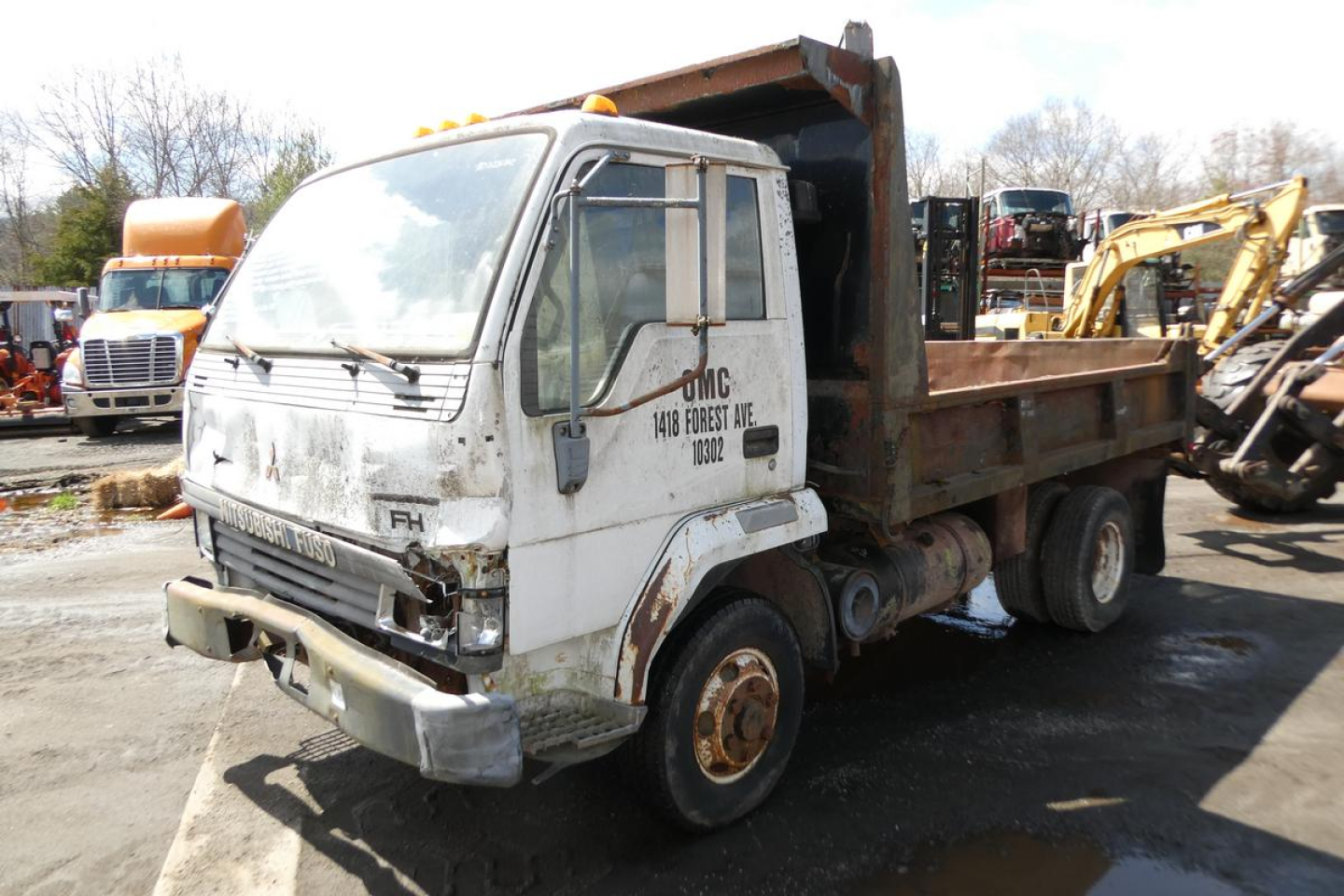 Dump truck cab and bed showing Mitsubishi FH model with white cab and rusted dump body, front view angled left.