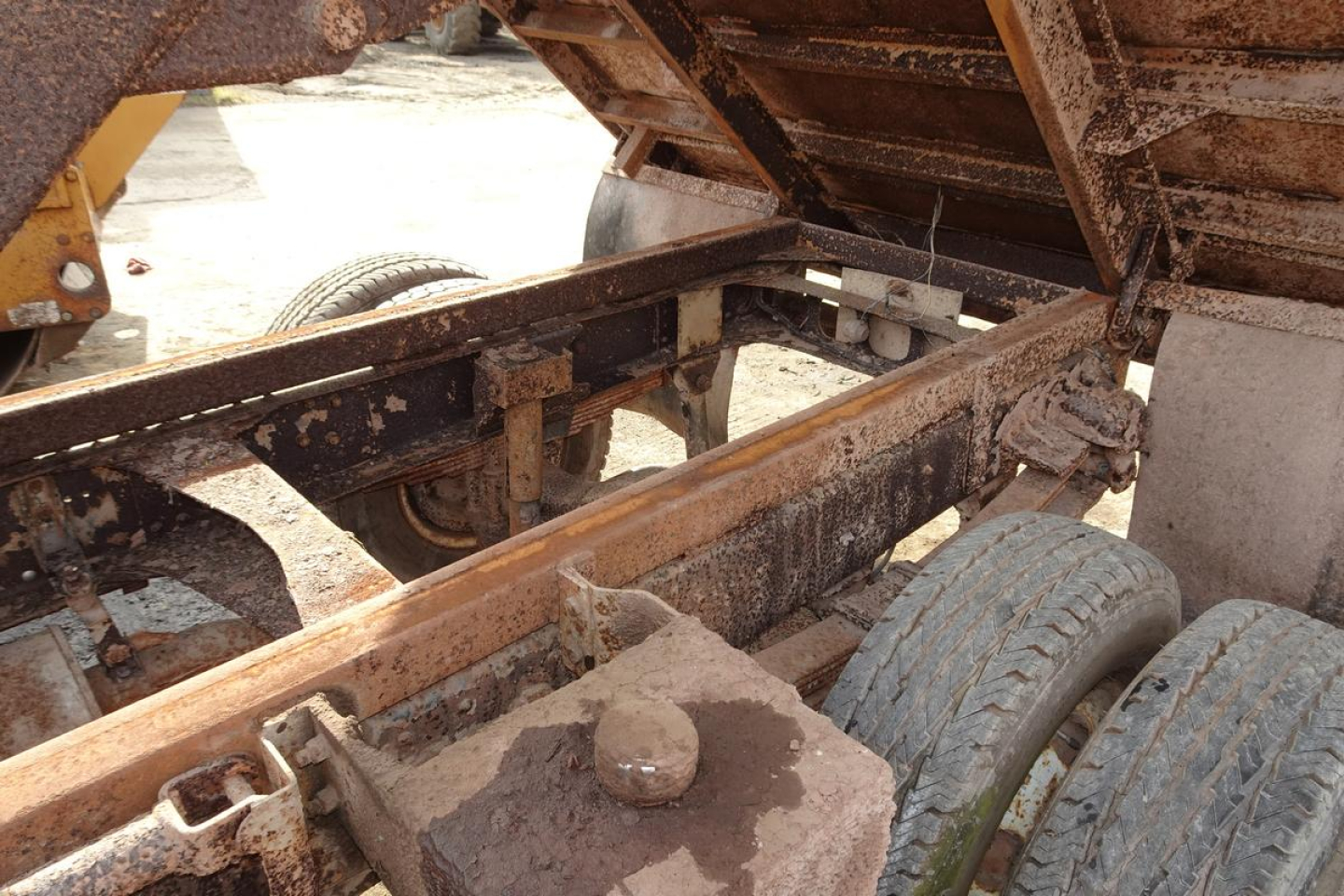 Dump truck chassis and bed showing rusted frame, dual rear wheels, and raised dump bed with hydraulic components visible.