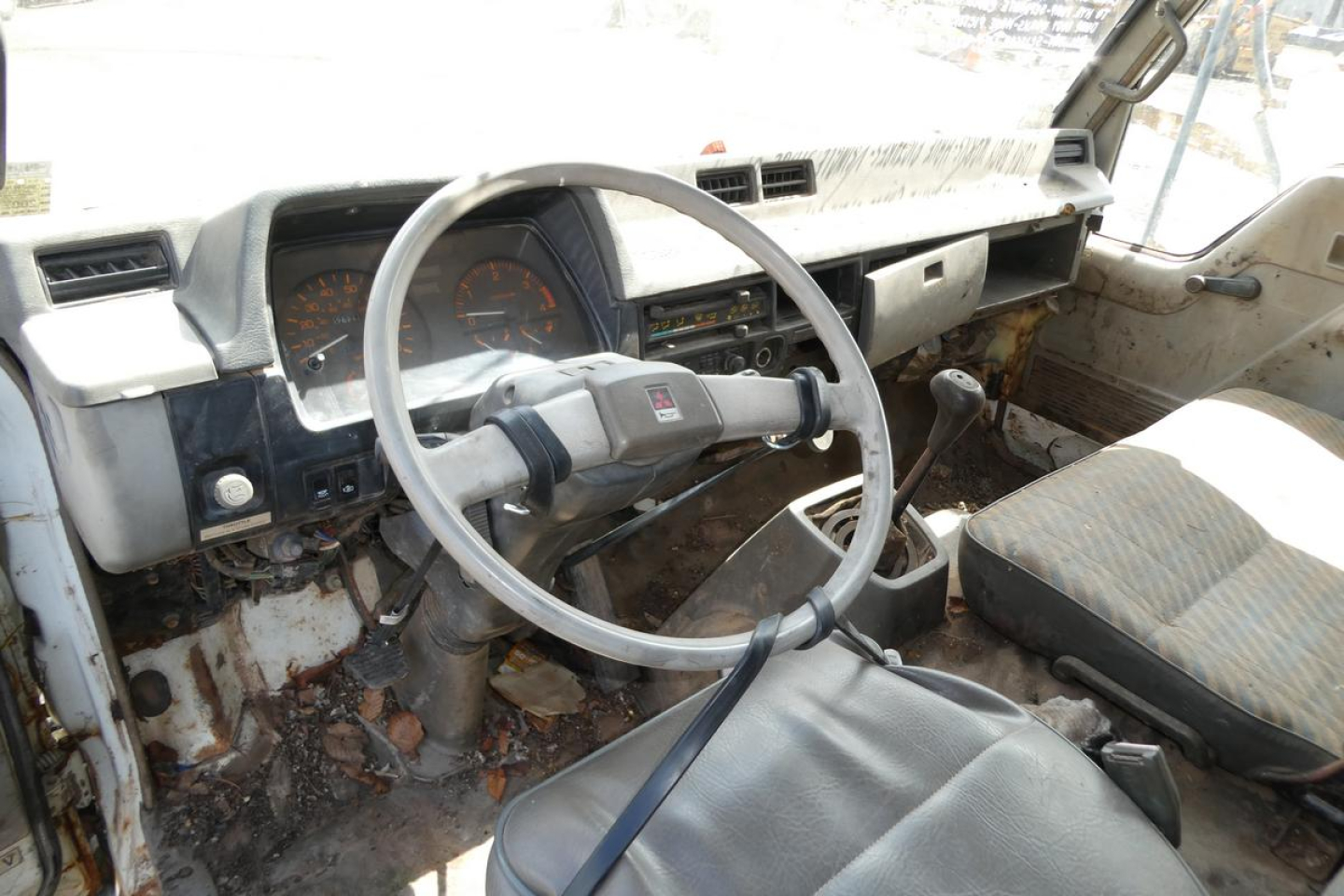 Mitsubishi FH dump truck interior showing steering wheel and dashboard with worn cabin area and exposed metal, dusty seats and manual shifter.