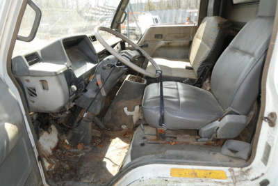 Interior of a 1993 Mitsubishi FH dump truck cab with steering wheel, dashboard, and front seats; worn floor area; visible wear and debris.