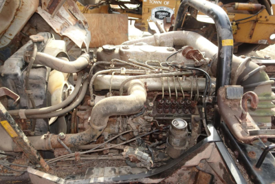 Truck engine bay showing fuel-injected diesel engine with multiple hoses and clamps in a dusty assembly area.
