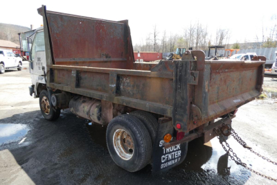 Dump truck bed showing rusted metal dump body and dual rear wheels with chain hitch and mud flaps.