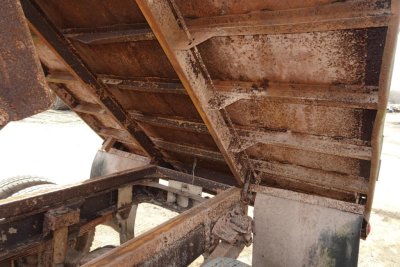 Dump truck bed raised showing rusty metal framework and hydraulic hinges.