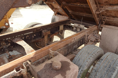 Dump truck chassis and bed showing rusted frame, dual rear wheels, and raised dump bed with hydraulic components visible.