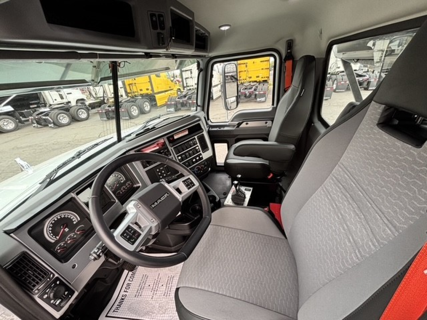 Interior view of a new 2026 Mack GR64B roll-off truck cab showing steering wheel, dashboard, seats, and controls.