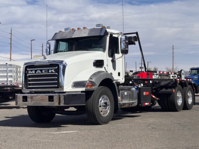 Mack GR64B cab and chassis truck in a parking lot, white cab, black chassis, chrome grille, Mack emblem, front bumper, dual rear axles, utility mirrors, warning lights on cab roof.