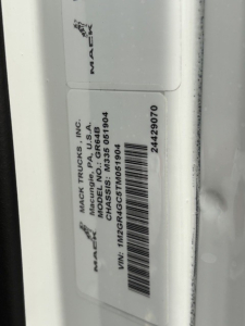 Mack GR64B chassis label and VIN sticker showing manufacturer and barcode. Text includes MAC TRU... MACK TRUCKS INC, MACK/P.A., USA, CHASSIS: M ... VIN: 1M2GR4GC5TM051904, stock number 24429070.