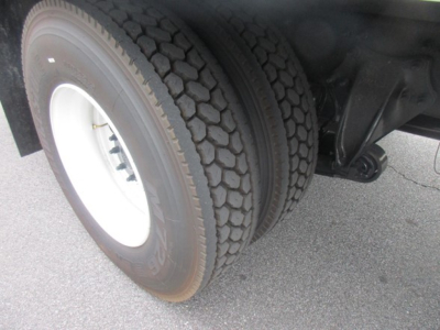 Truck rear wheel and suspension showing dual tires and axle components with black undercarriage and concrete ground.