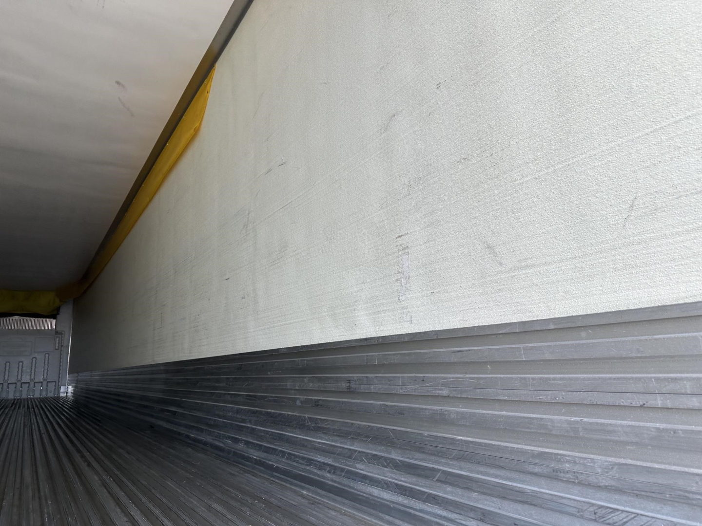Trailer interior showing metal ribbed floor and side wall, with a yellow upper edge and ribbed aluminum curb; empty cargo space.