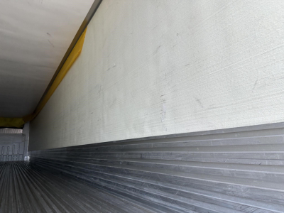Trailer interior showing metal ribbed floor and side wall, with a yellow upper edge and ribbed aluminum curb; empty cargo space.