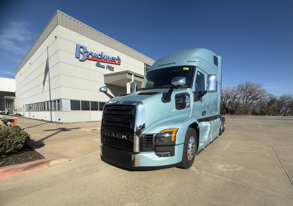 Mack PR64T76H conventional sleeper truck in light blue parked outside dealership