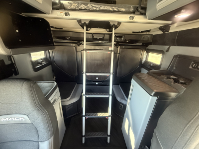 Truck cab interior with a metal ladder leading to a loft area; visible branding includes 'MACK' on a seat; various cabinets and a sink module in dark gray/blue colors.