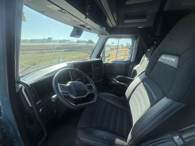 Interior of a new Mack PR64T76H truck cab showing steering wheel, passenger seat with Mack logo, dashboard, and windshield.