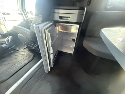 Interior cab area of a 2026 Mack PR64T76H showing an open compact refrigerator/freezer unit under the dash.