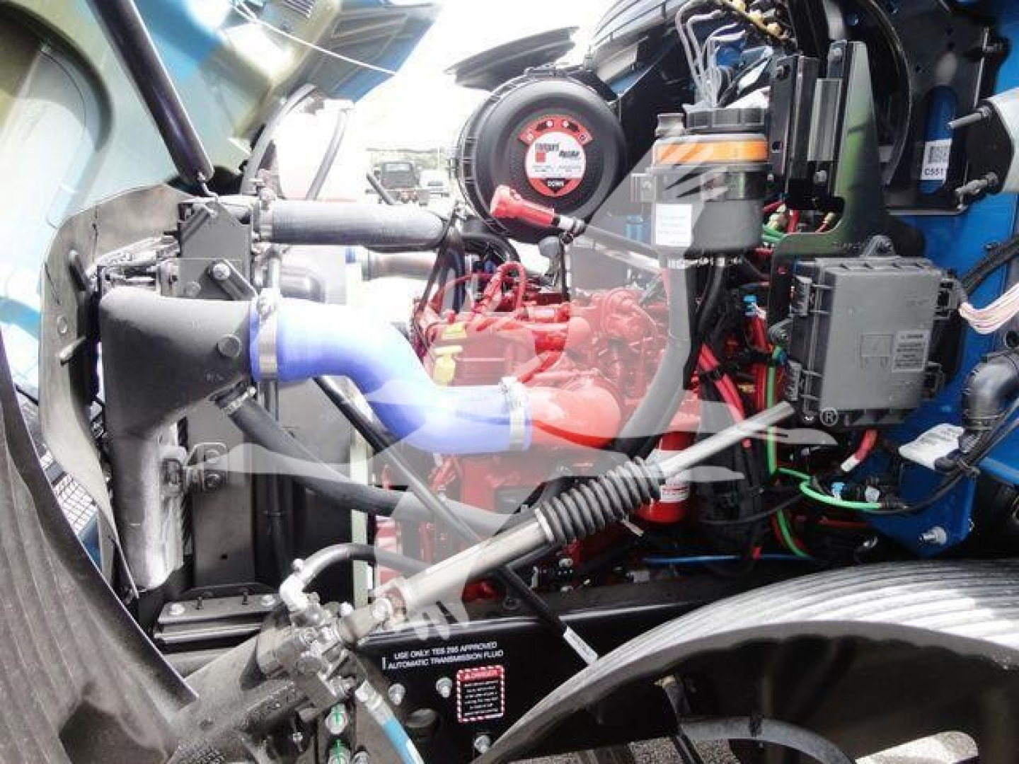 HD engine bay image of a 2027 Mack MD6 rollback truck showing engine components, hoses, wiring, turbo, radiator area, and label stickers.