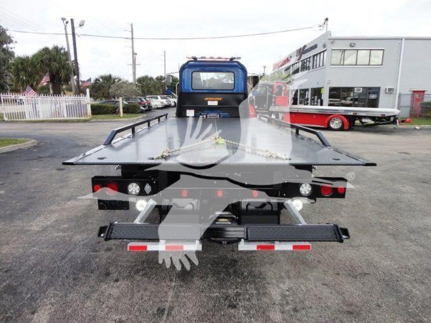 Truck bed with rooftop car carrier and rearview of a Mack MD6 rollback -- flatbed with hydraulic bed and taillights visible.