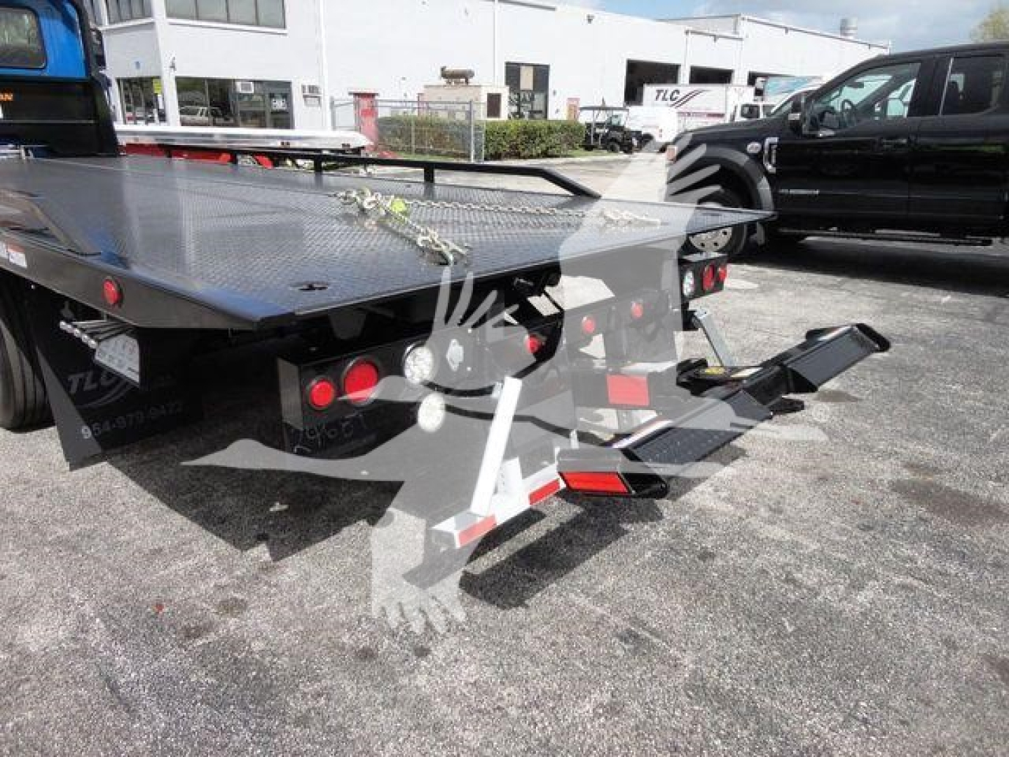 Truck bed with hydraulic rollback equipment on a 2027 Mack MD6 seen from rear-left, flatbed platform with accessibility ramps and hydraulic components.