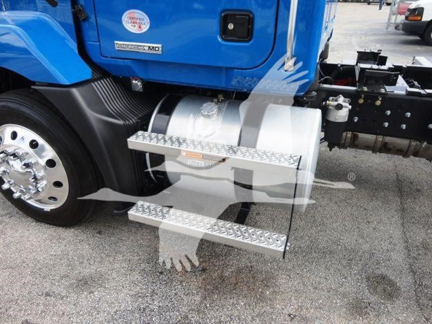 Truck cab side with chrome dual-step access platform attached, blue Mack MD6 undercarriage visible, wheel and fuel tank area seen.