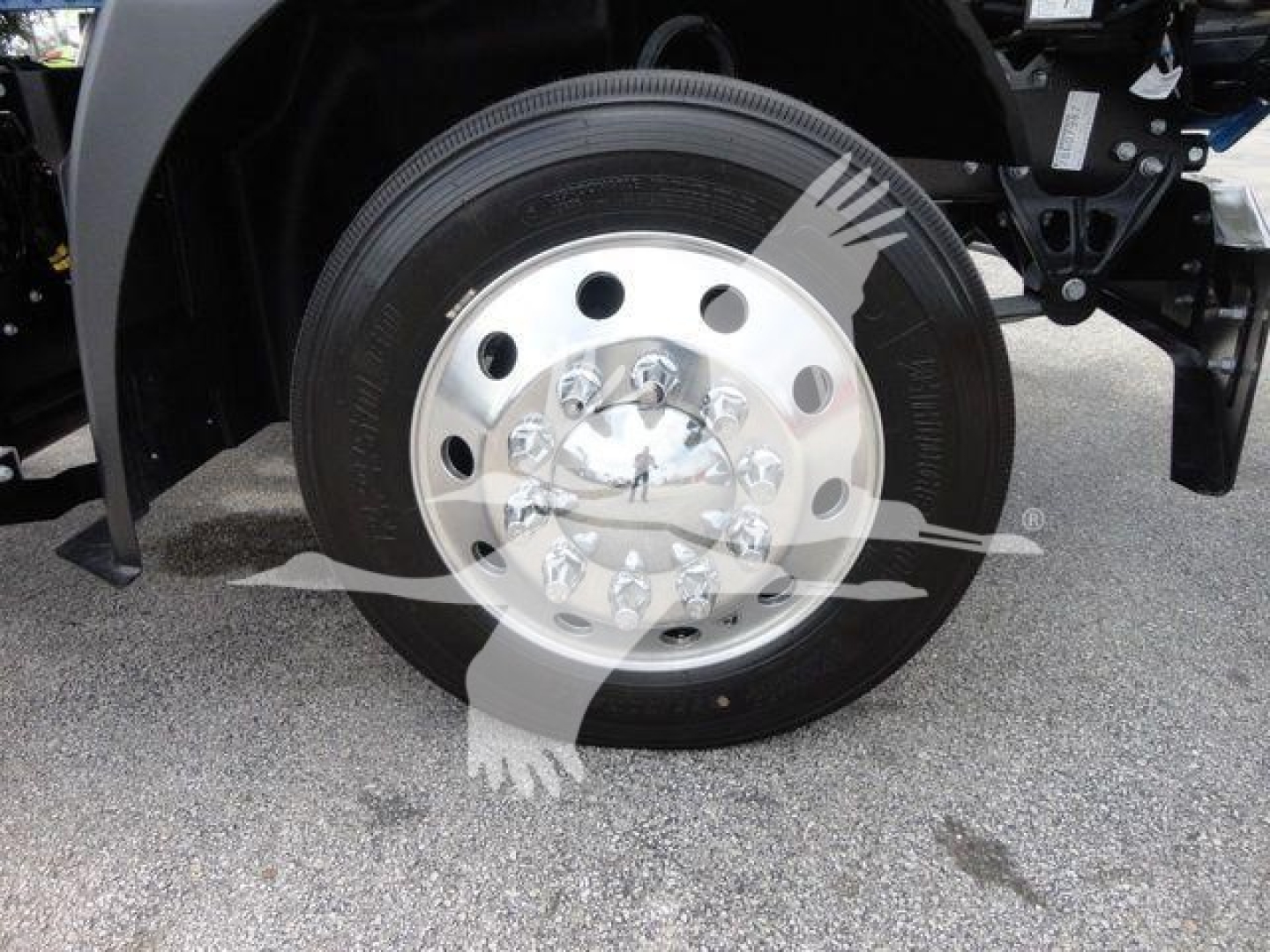 Truck front wheel and hub showing steel wheel with multiple circular holes and black tire under Mack MD6 rollback truck.