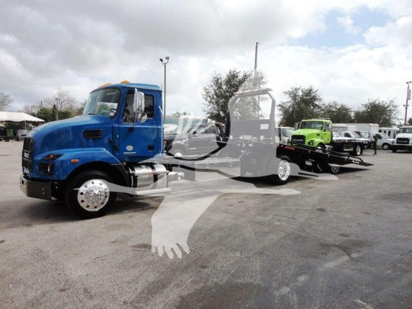 Blue Mack MD6 truck in a rollout yard with a flatbed trailer and other trucks in background, stock number J04369.