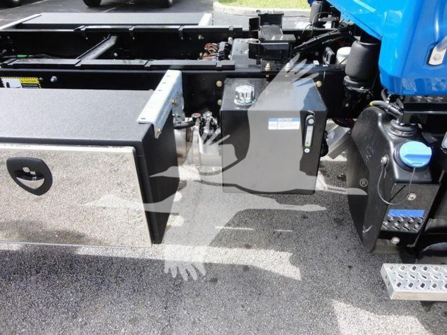 MD6 truck chassis side view showing toolbox, frame rails, and blue cab portion with steps and hydraulic lines.