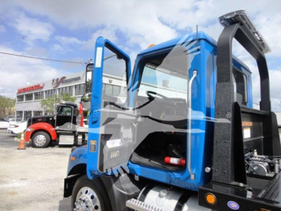 MD6 truck cab open door view showing blue cab and black rollback equipment mount with hydraulic component and ladder, foreground engine bay area visible.