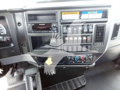 Dashboard of a Mack MD6 truck showing stereo, climate controls, hazard switches and a yellow key tag; various warning labels and control panels visible.
