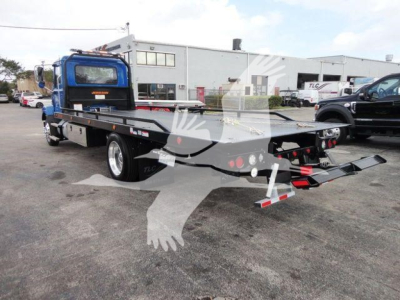 Flatbed rollback tow truck with blue cab and black flatbed showing hydraulic ramps and rear lights.