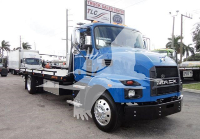Flatbed tow truck in blue and gray with Mack logo, front view showing cab and wheel, dealership lot in background.