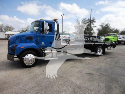 Blue Mack MD6 tow truck in a lot with flatbed and another green truck in the background.