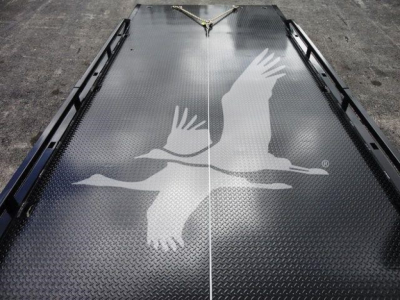Flatbed/haulbed with textured diamond plate surface showing a white silhouette of two flying birds along the center crease, with side rails and tie-downs visible.