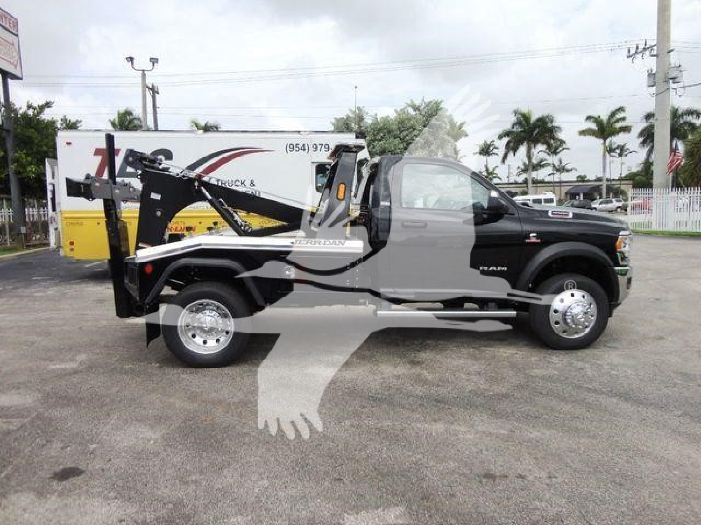 Ram 4500 tow truck chassis with wheel-lift on bed, side view showing winch equipment and cab; Ram badge visible; dealership lot in background.