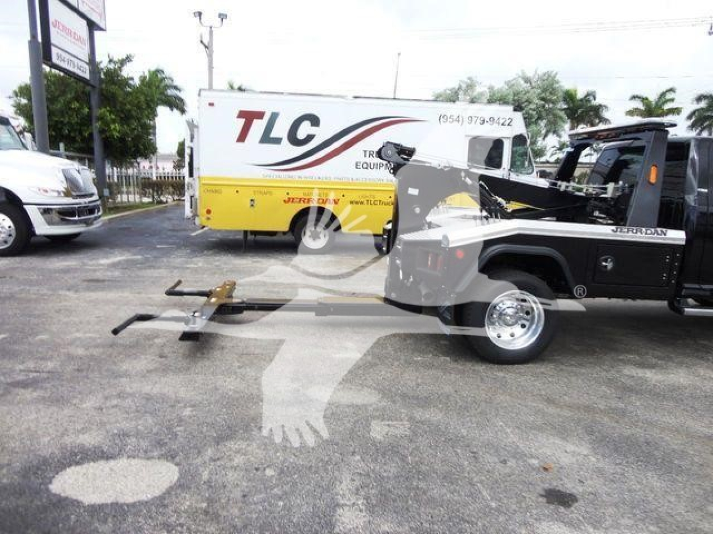 Ram 4500 tow truck in a parking lot with a wheel-lift and winch equipment attached, black cab, yellow TLC equipment truck in background.