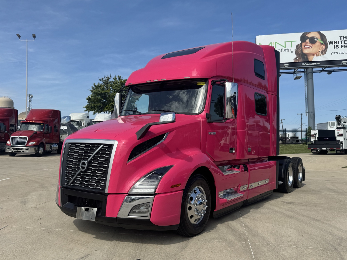 Volvo VNL64T860 tractor in pink color with sleeper cab, front grille, headlights, and side mirrors visible.