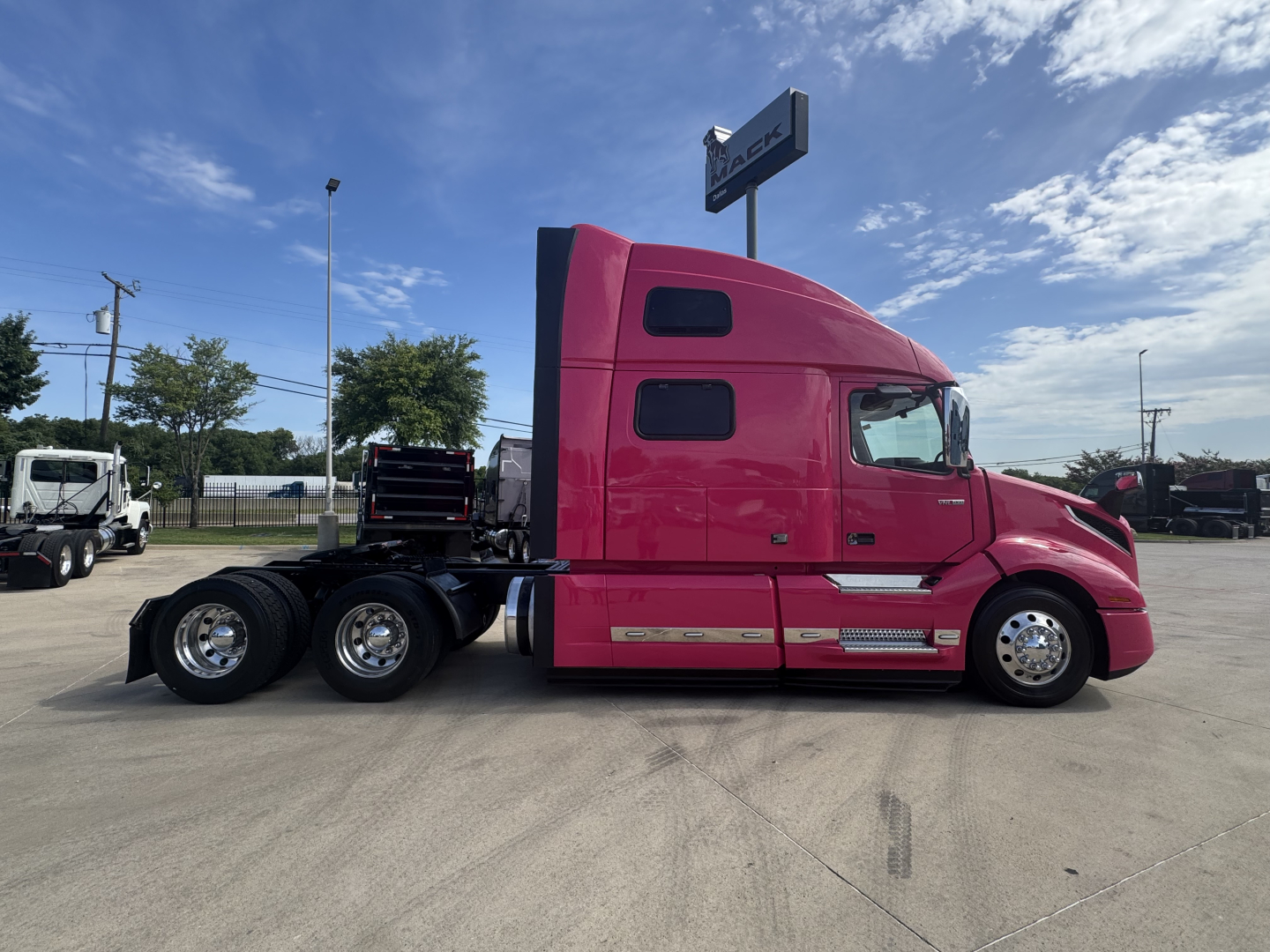 Side view of a pink Volvo VNL truck tractor with sleeper cab, showing rear axles and chassis, no visible text on cab side.