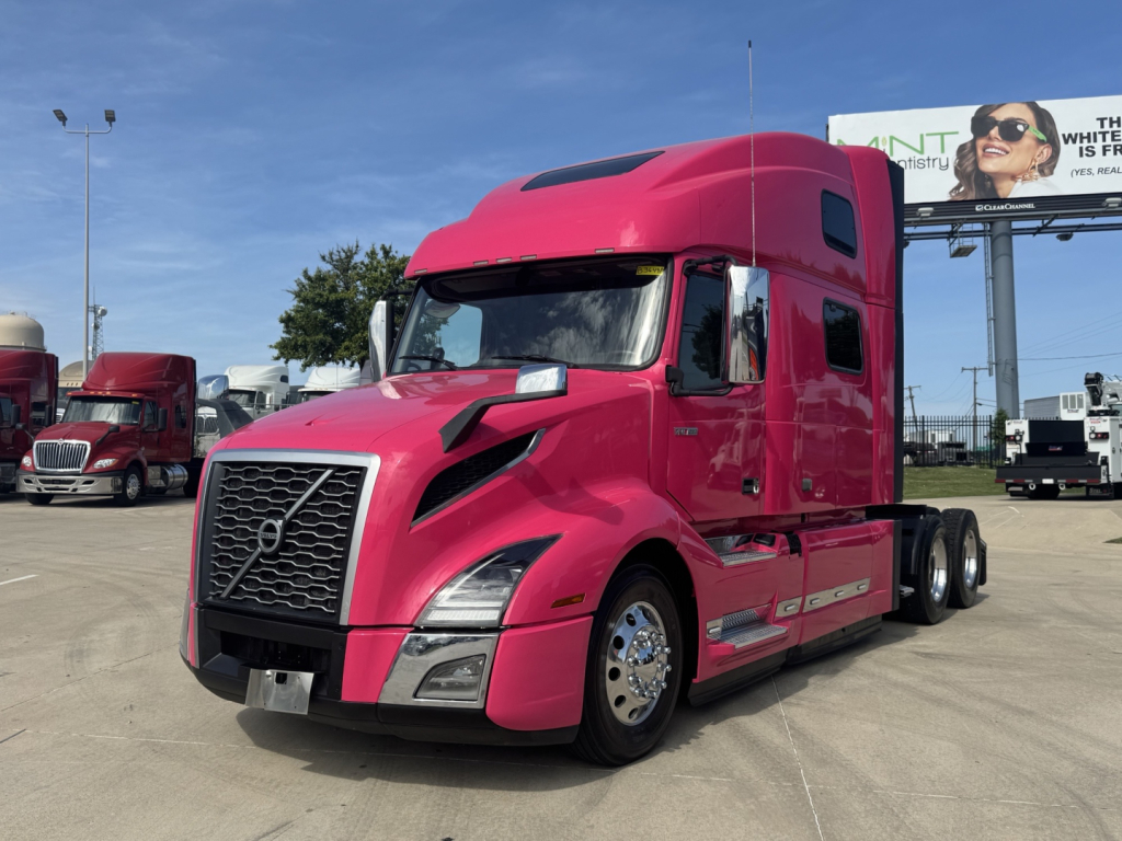 Volvo VNL64T860 tractor in pink color with sleeper cab, front grille, headlights, and side mirrors visible.