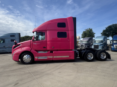 Side view of a pink 2023 Volvo VNL64T860 tractor with sleeper cab, showing the long hood, aerodynamic mirrors, and dual rear axles.