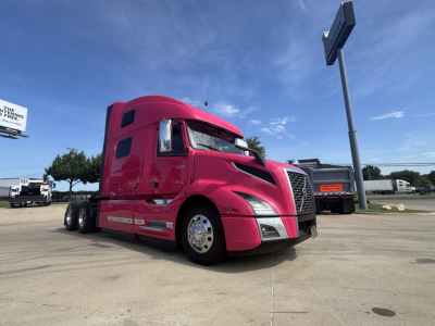 2023 Volvo VNL64T860 tractor-trailer in pink color, front-left view, showing sleeper cab, chrome wheels, and aerodynamic design under clear sky.