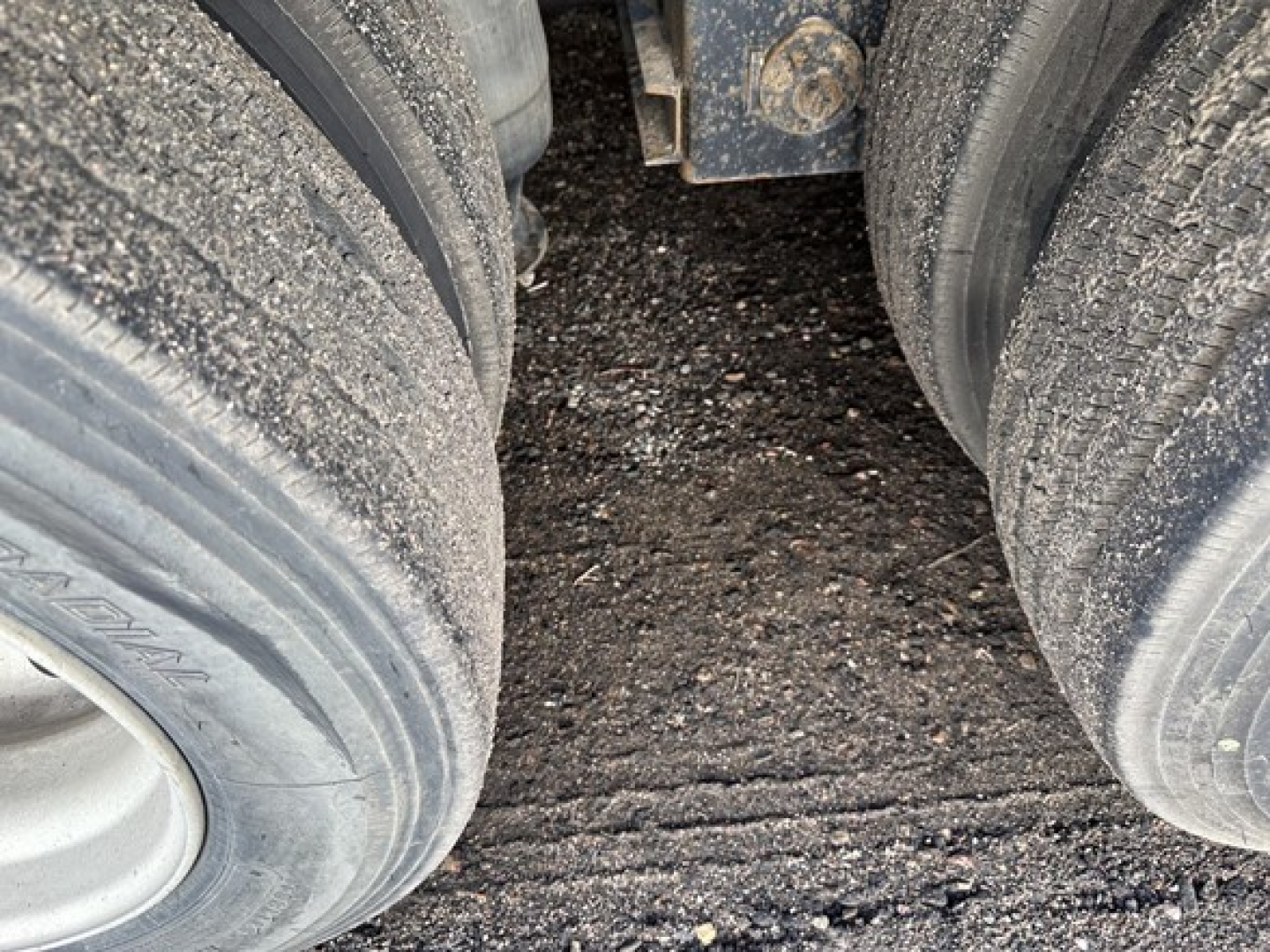 Trailer axles and tires view under a 40-ton hydraulic tail trailer showing dusty dual rear wheels and mud, with some frame and hitch hardware visible.