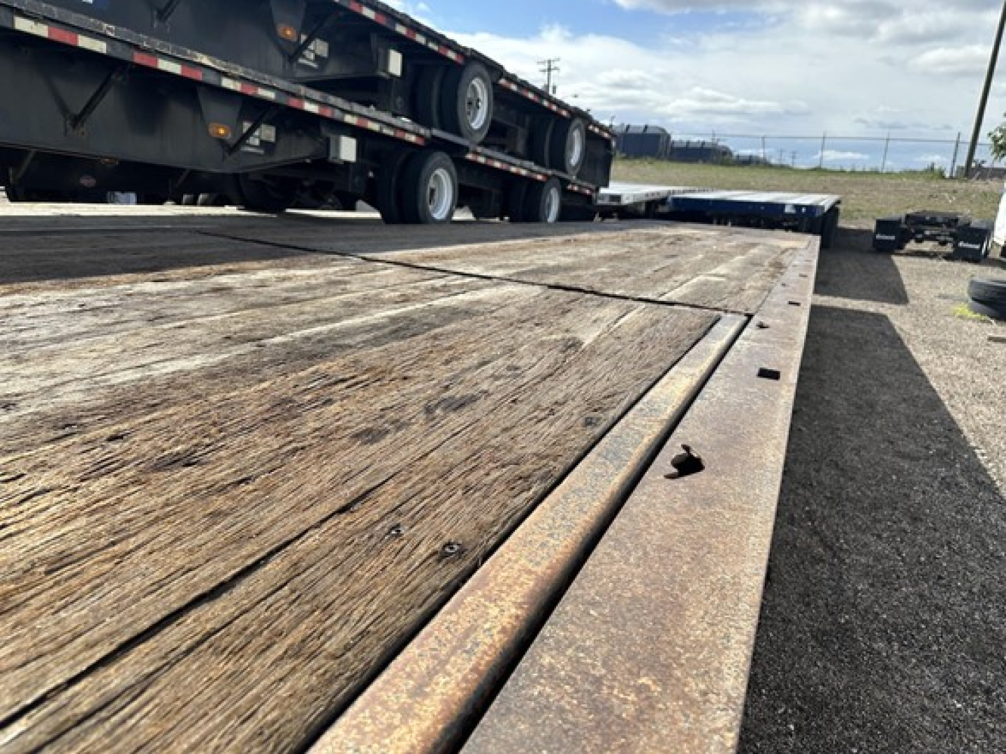 Trail King 40 Ton hydraulic tail trailer deck with wooden planks and rusted metal edges; flatbed area in foreground; other trailers and tires visible in background.