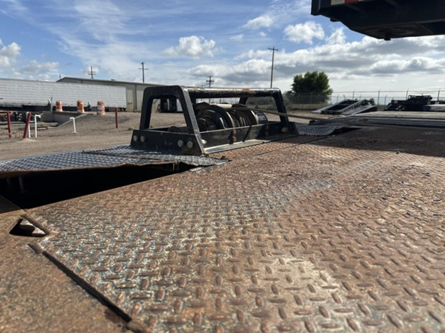 Flatbed trailer deck with diamond plate surface and a metal guard rail. View shows rear area with winch and open deck cutouts. Text not legible in this image.