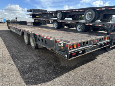 Trailer 40-ton hydraulic tail flatbed showing dual rear axles with wooden deck and stacked trailers in background.