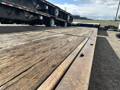 Trail King 40 Ton hydraulic tail trailer deck with wooden planks and rusted metal edges; flatbed area in foreground; other trailers and tires visible in background.